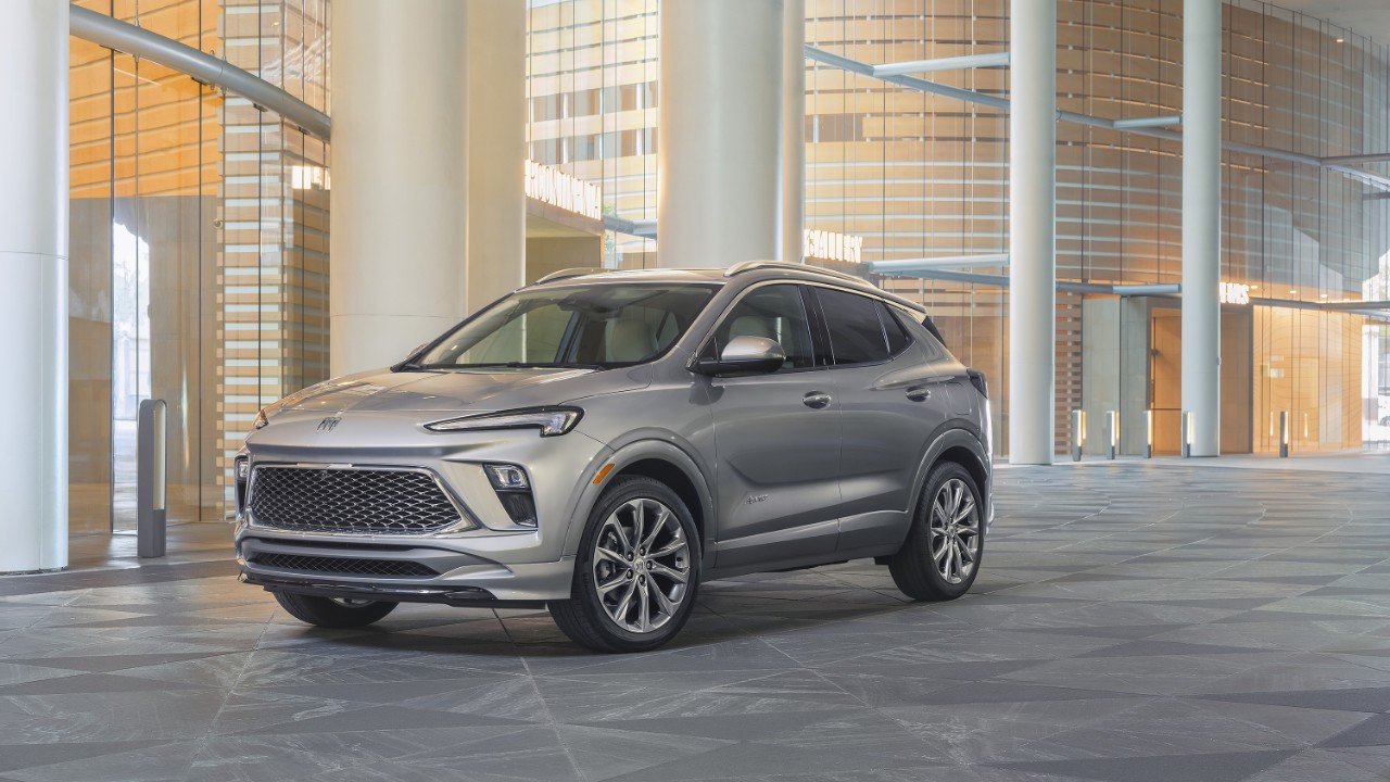 Buick Encore GX Avenir in Moonstone Gray Metallic is parked in front of a modern building.