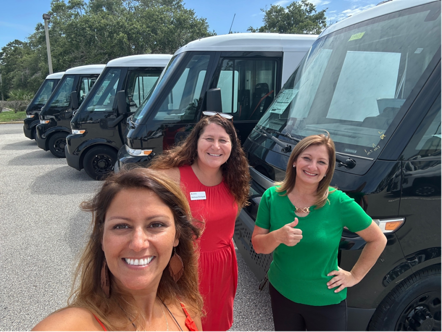 Three people in front of five BrightDrop vans