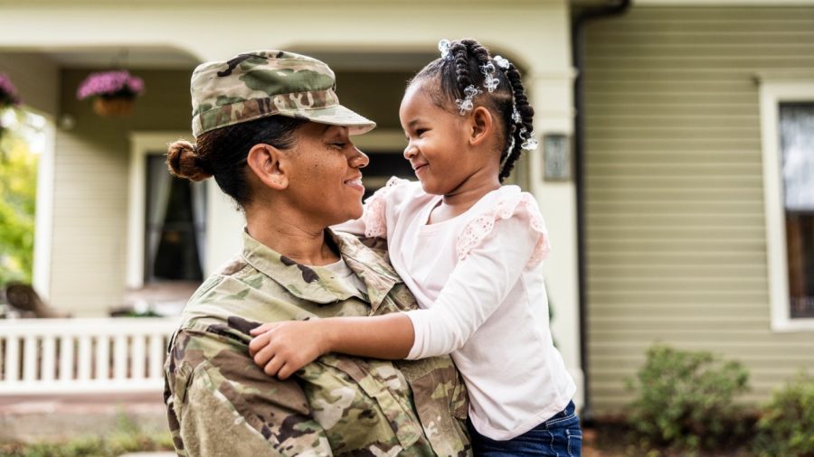Portrait of female U.S. soldier in uniform with young daughter in front of home