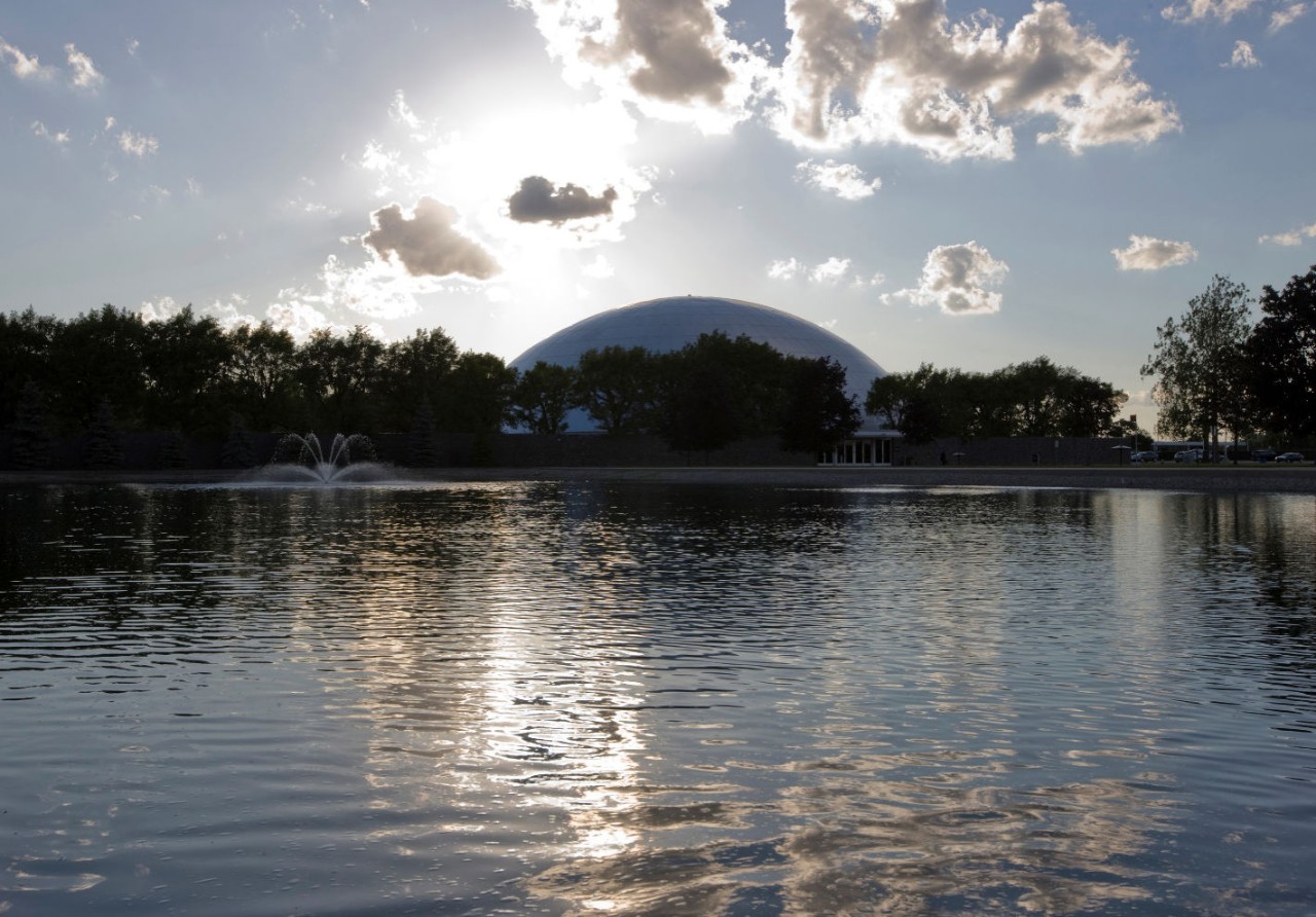 A body of water with trees and the GM Design Dome in the background