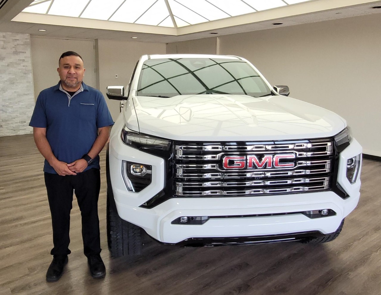 GM employee Erick Sanchez stands next to a white GMC Canyon truck in a brightly lit lobby area.
