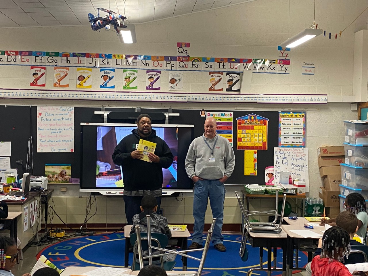 Two GM employees in front of a classroom discussing a children's book featuring science, technology, engineering, and math.