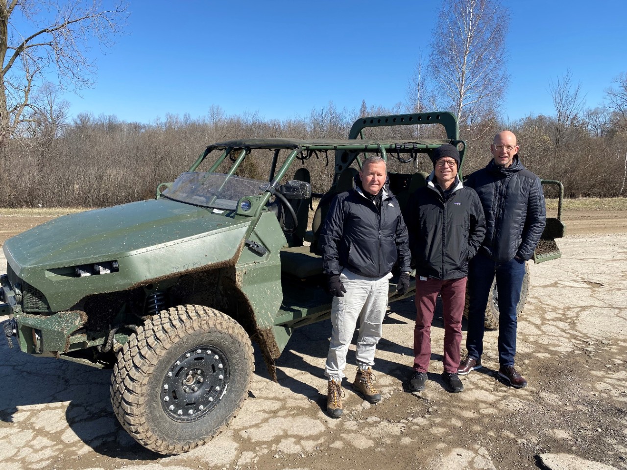 A group of men standing in front of a green utility vehicle.