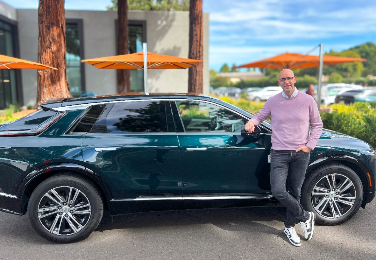 A man in a pink sweater leaning on a green car