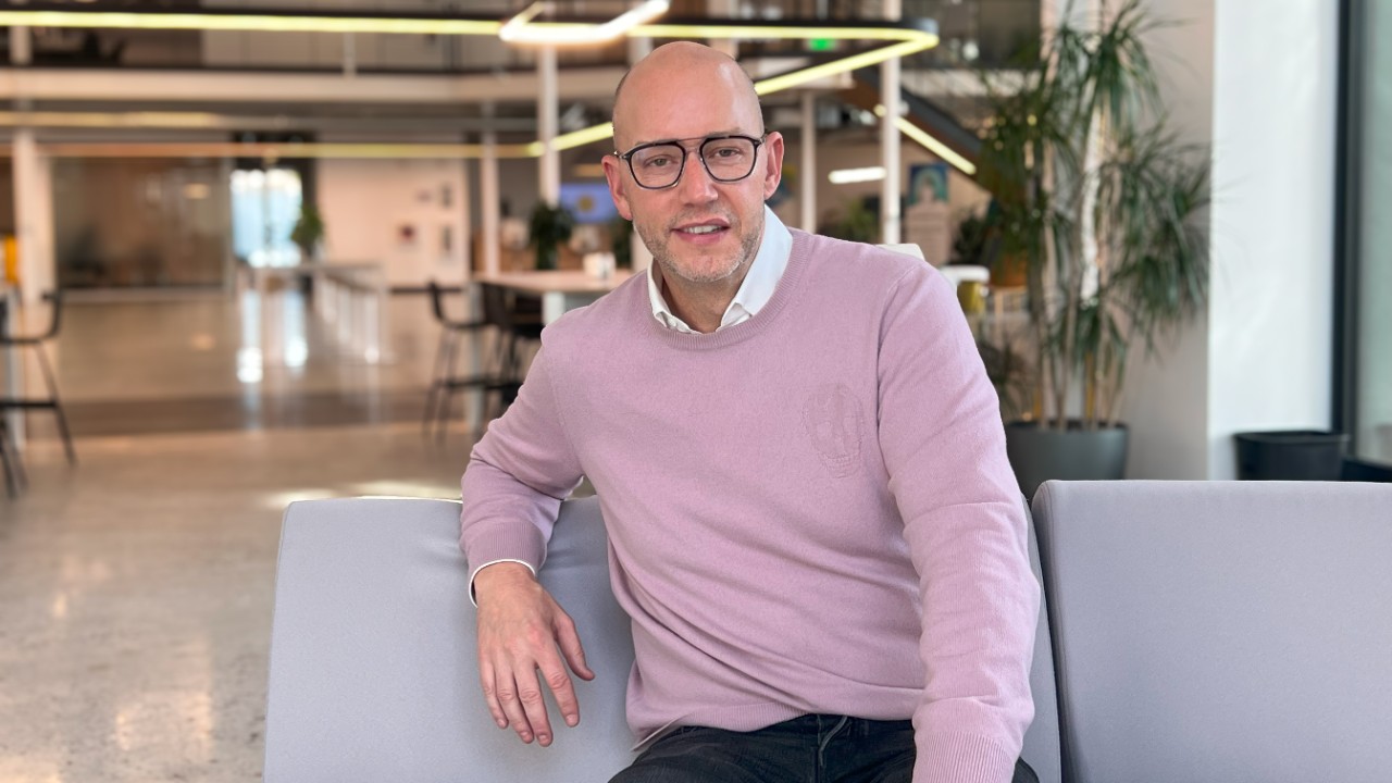 A man in a pink sweater sitting on a couch.