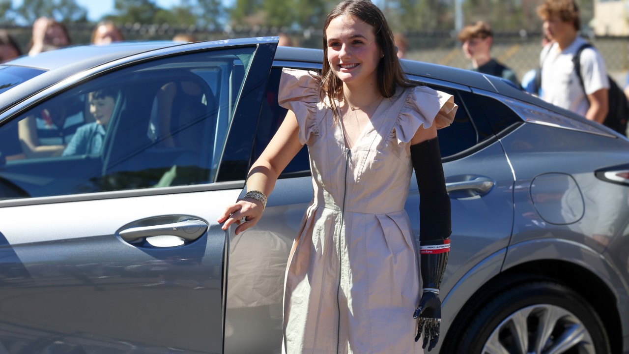 A teen girl smiling in front of a car.