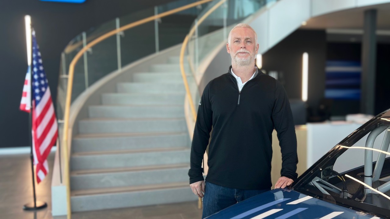 Anthony Heenan standing in front of a race car in an office lobby.