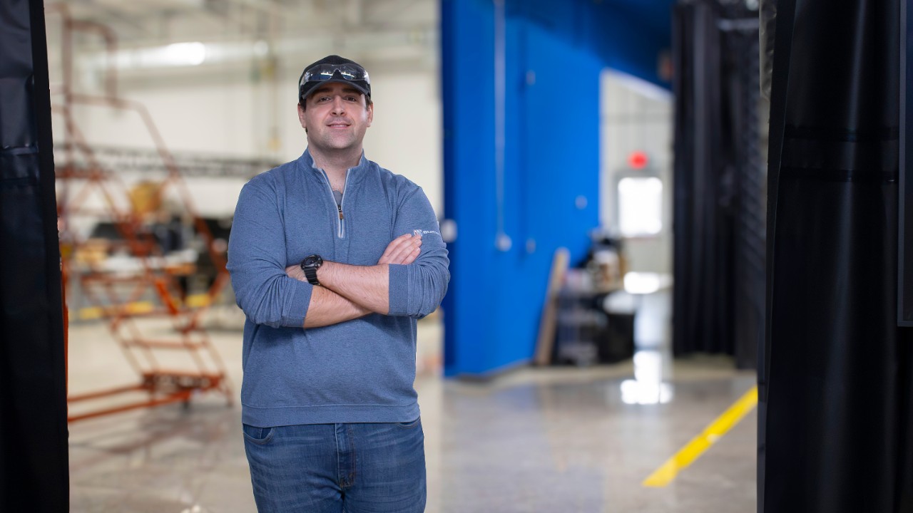 Max Sikorski wears a blue quarter-zip, jeans and a black baseball cap while standing in the virtual reality lab surrounded