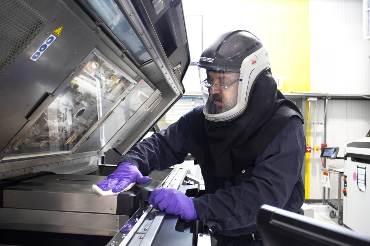 Metal model maker Jason Blackburn wears navy coveralls, a ventilated helmet, and purple gloves