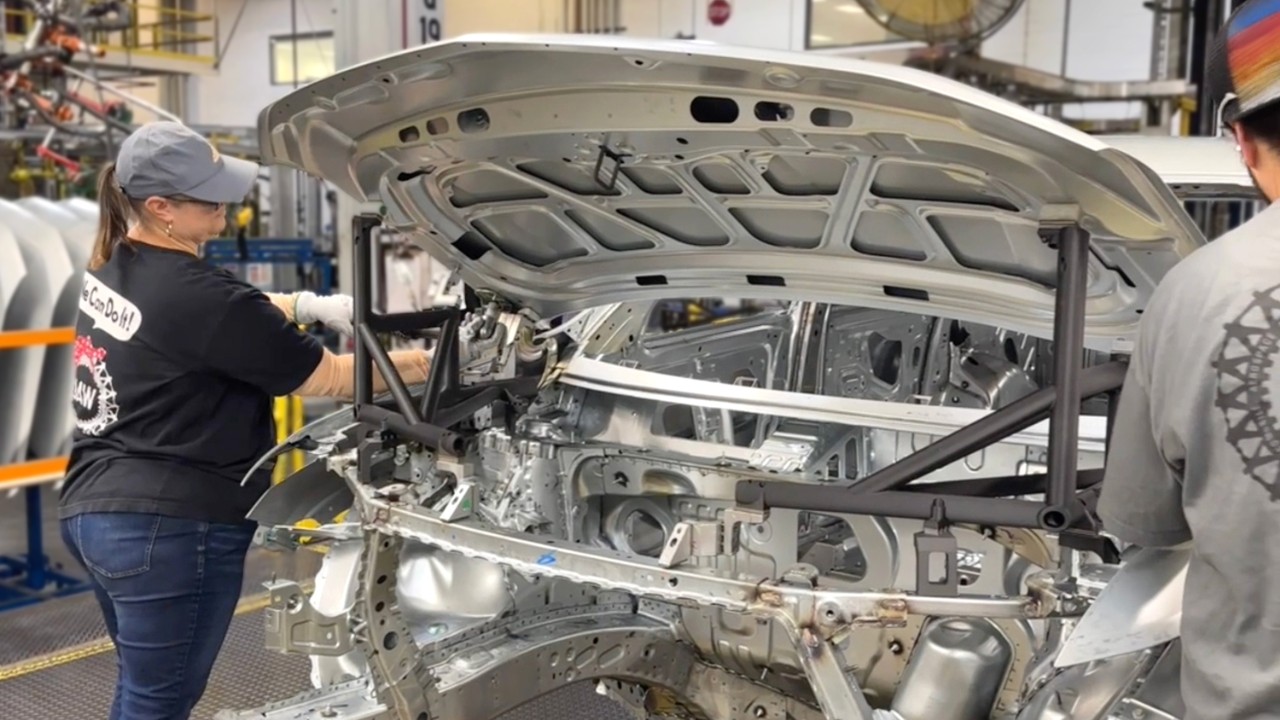 Lansing Delta Township team member Kayla Dubois uses a 3D printed hood fixture (dark gray beam) on her station.