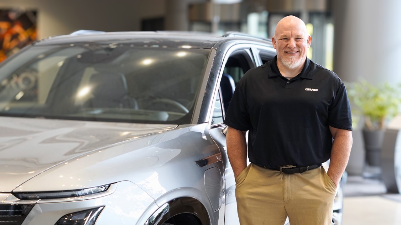 A smiling man stands in front of a Cadillac EV
