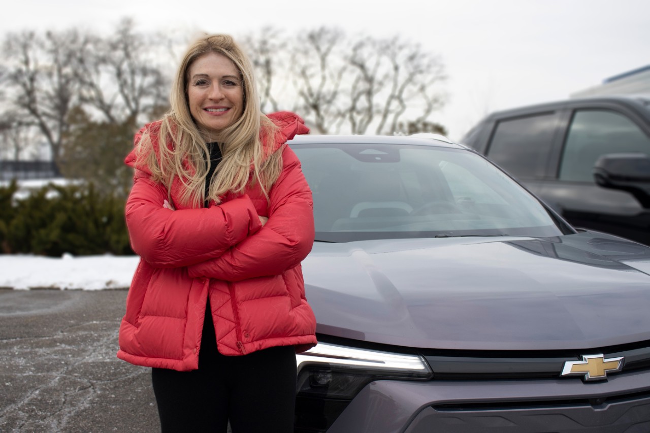 Chief engineer Marisa Cullens wears a pink puffer coat and stands front of a dark red Chevy Equinox EV.