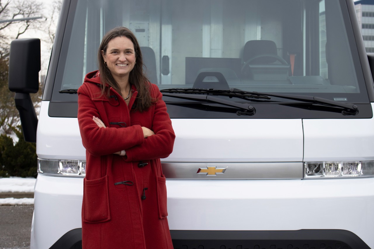 Chief engineer Joan Petit wears a bright red coat and stands in front of a white Chevy Brightdrop electric van.