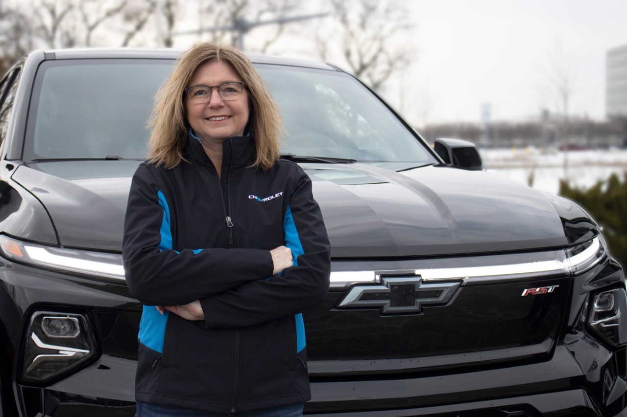 Chief engineer Kathy Gillespie wears a black and bright blue Chevy EV jacket and stands in front of a black Silverado EV.