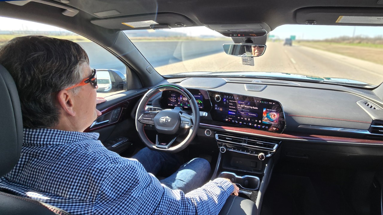 Man in a checkered shirt driving a car.