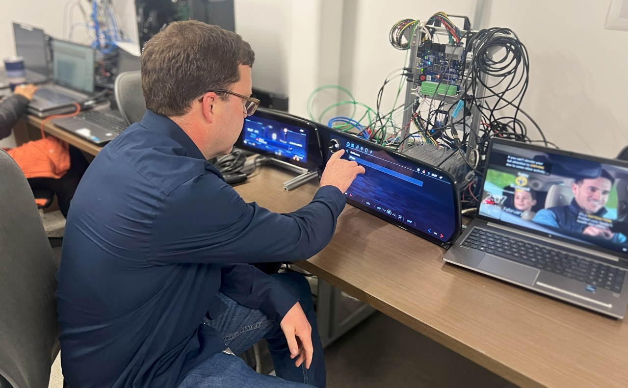 A man in a navy shirt sitting at a desk with multiple monitors.