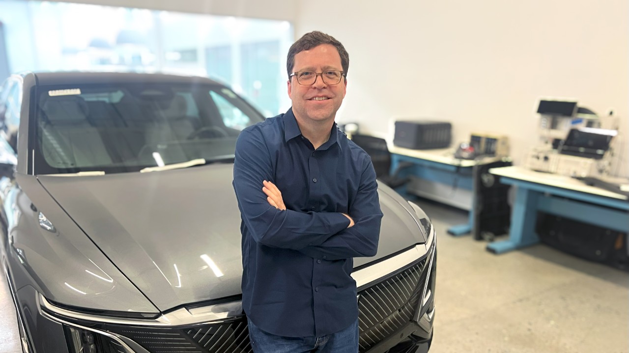 A man in a navy shirt standing in front of a silver car.