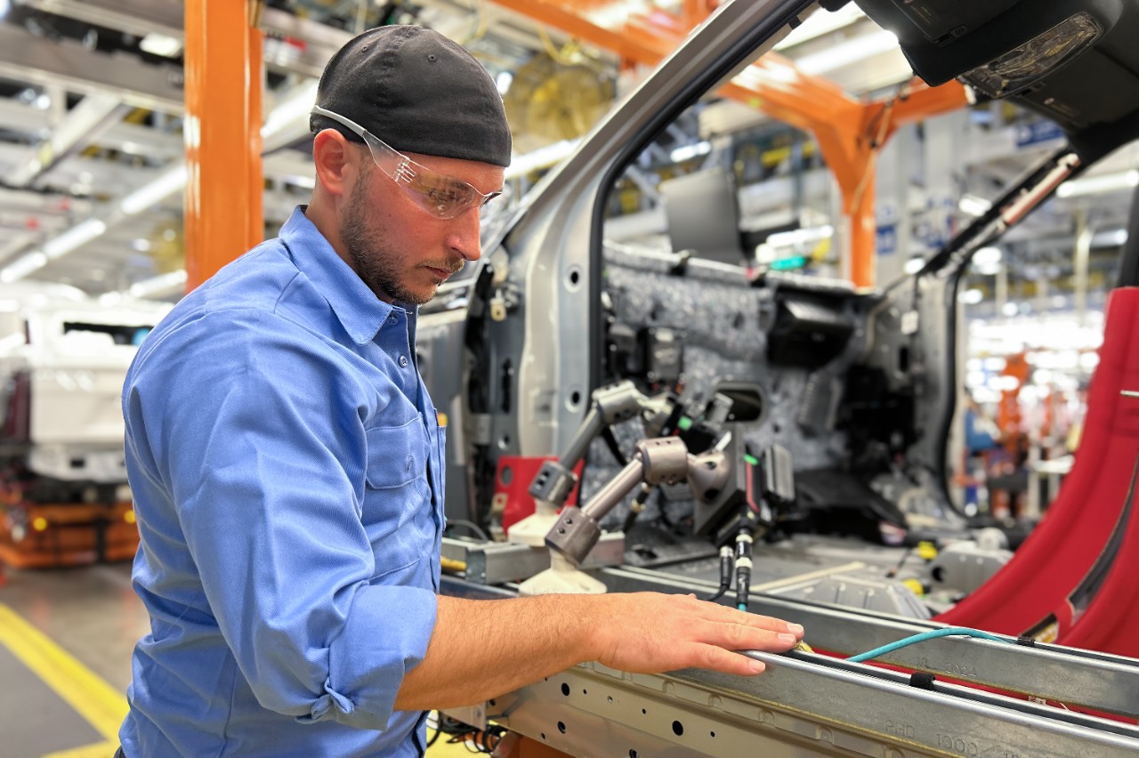 A man works on a vehicle on an assembly line.