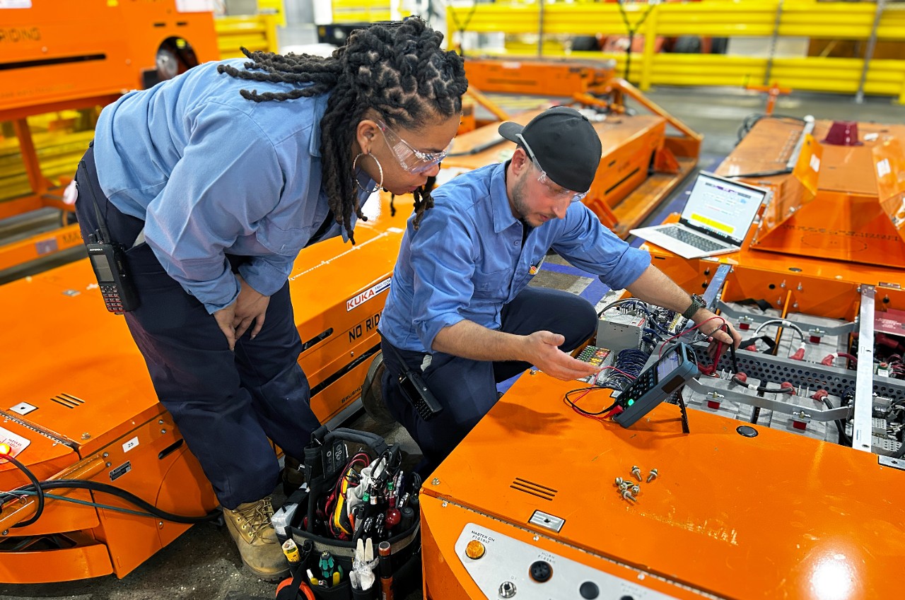 Factory ZERO electrician apprentice Tracie Leggs (left) works alongside Thompson (right) A man and woman work on an assembly line.