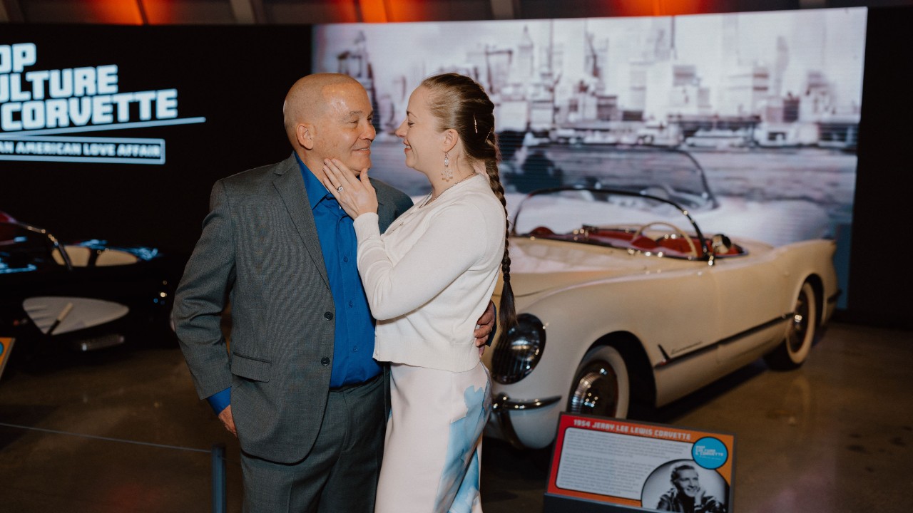 A couple embrace in front of a car.