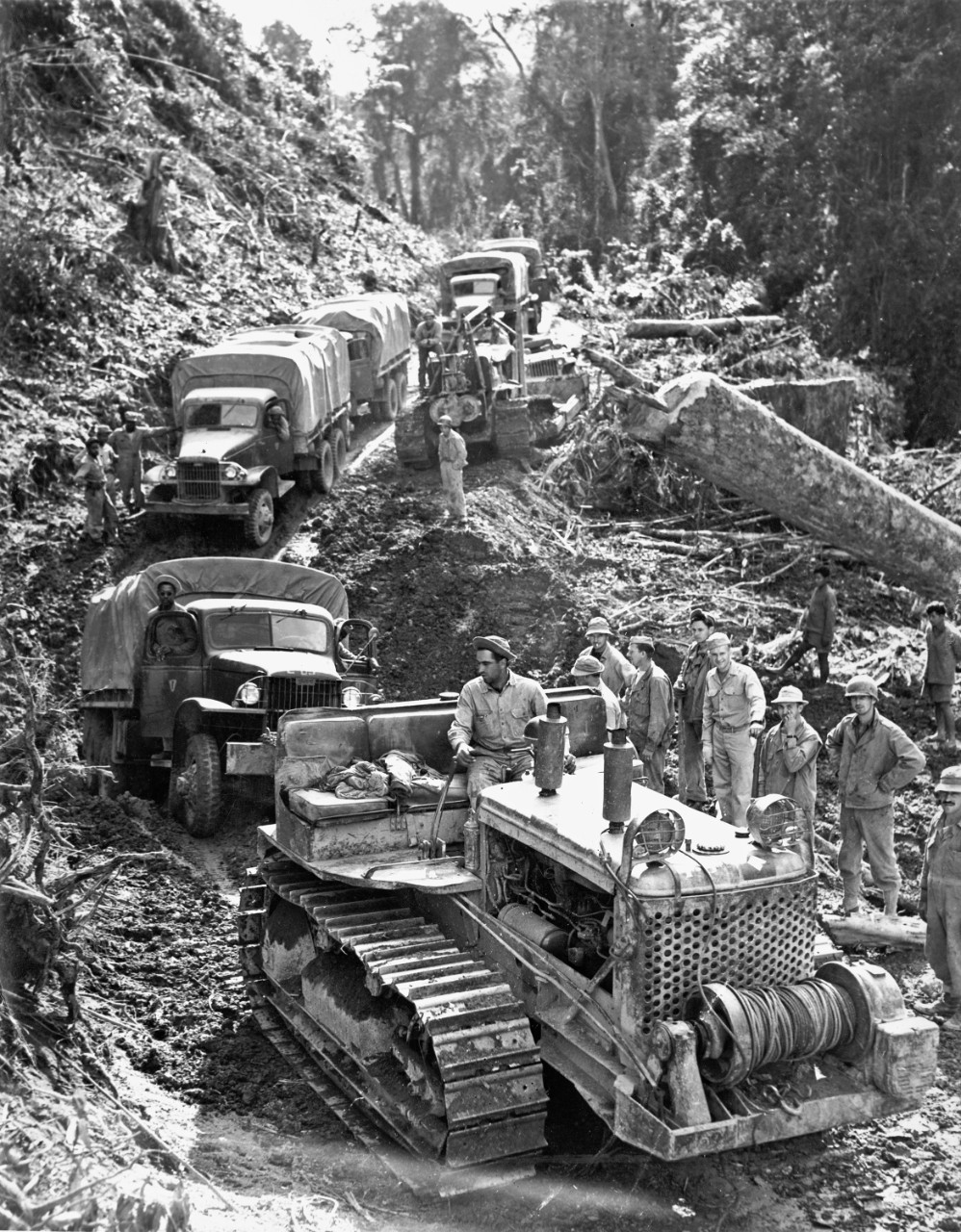 Led by a bulldozer, a line of GM trucks works through the mud.