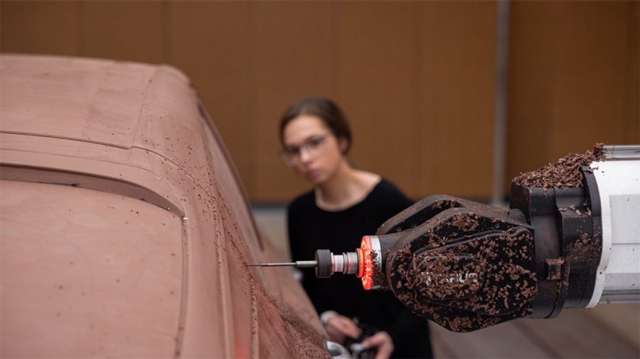 Car designer observes machine shaping clay.