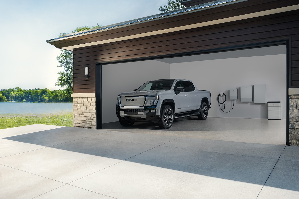 GMC Sierra EV Denali parked in residential garage alongside GM Energy Home System mounted on garage wall.